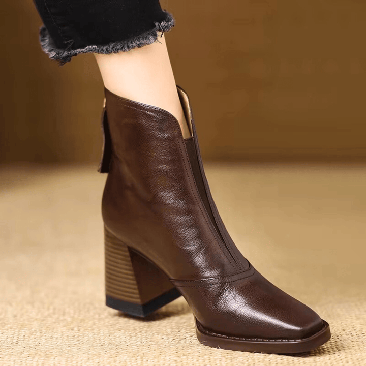 A woman in tailored pants wearing polished mid-heel ankle boots with a back zip.