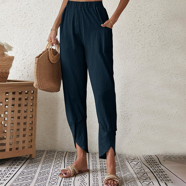 Woman wearing tapered pants with a slit hem at the ankle, walking near the coast.