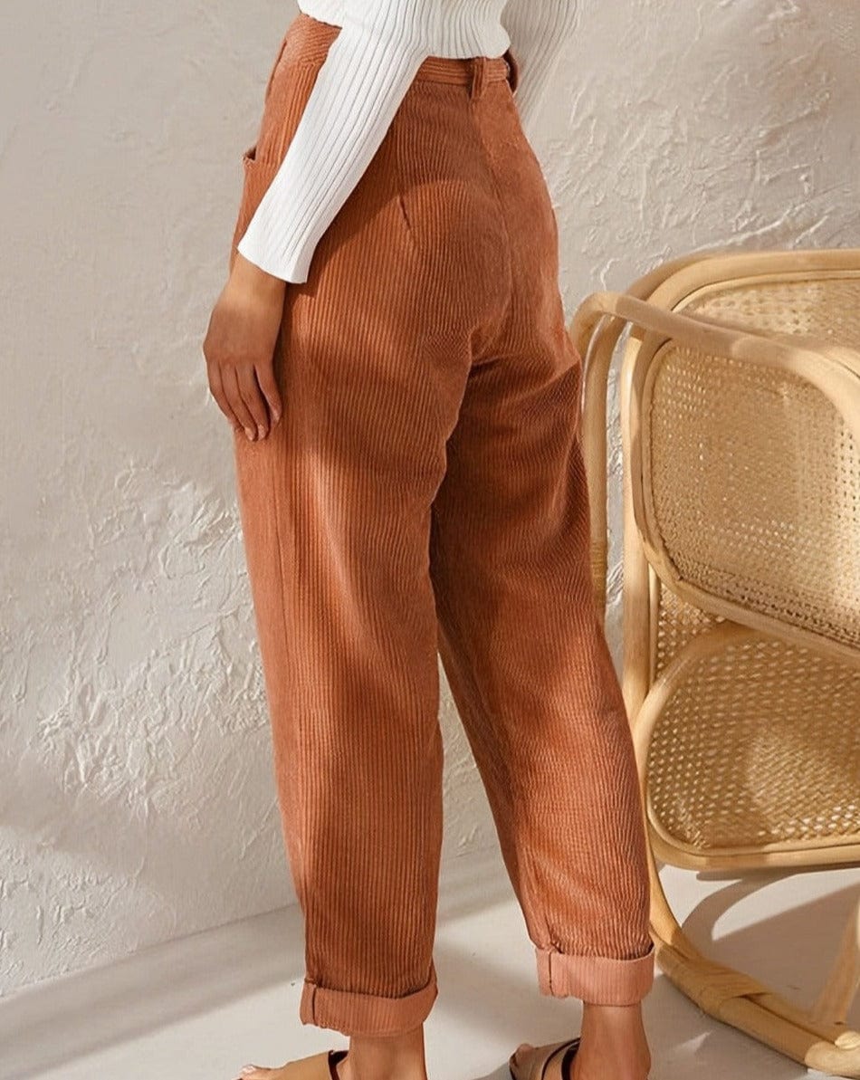 Woman wearing loose high-waisted pants with a tucked-in top, standing in soft light.