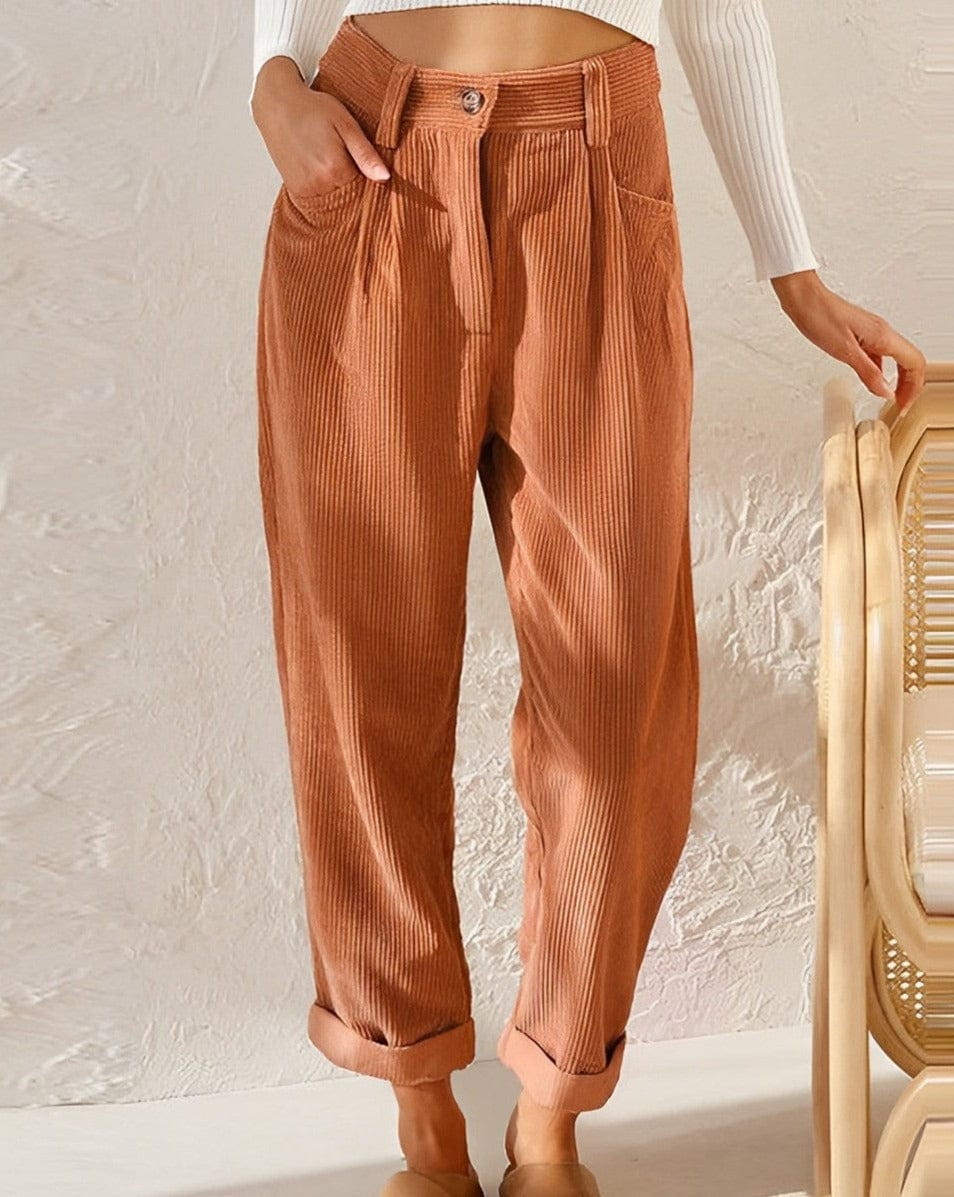 Woman wearing loose high-waisted pants with a tucked-in top, standing in soft light.